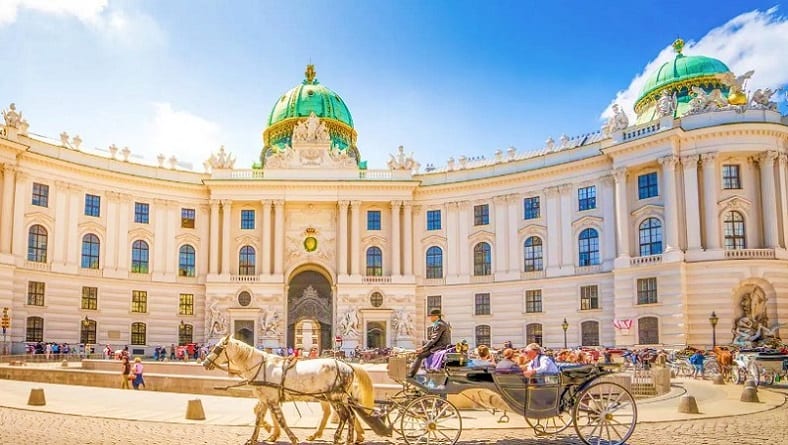 Horse-drawn carriage in front of Hofburg Palace courtyard with cream-colored baroque architecture and green copper dome in Vi
